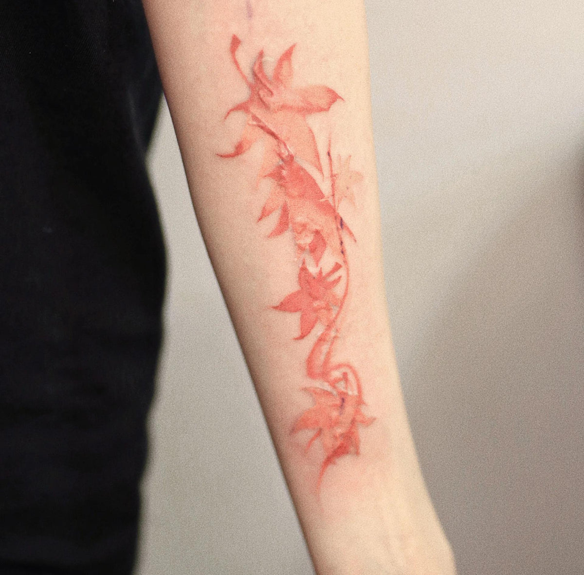 Delicate red maple leaf tattoos on an arm